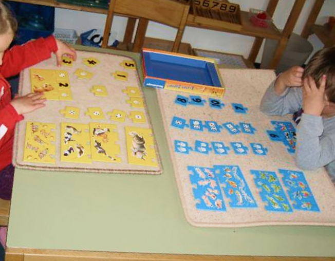 Zwei Kinder legen an einem Tisch gelbe und blaue Zahlen- und Bildkarten auf Teppiche