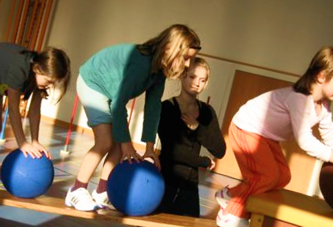 Kinder und eine Betreuerin stützen sich in der Turnhalle auf grosse blaue Gymnastikbälle